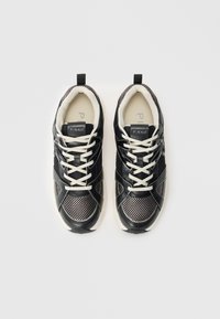 Baskets en mesh et cuir noir et gris avec des lacets blancs et du branding, présentant un dessus texturé et un col souple et rembourré.