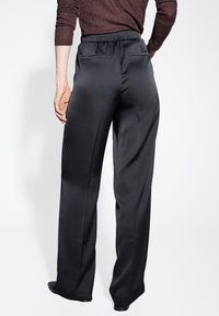 Pantaloni neri a gamba larga realizzati in tessuto liscio, con vita elasticizzata arricciata e due tasche posteriori. Design a lunghezza intera.