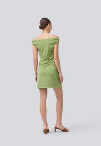 Abito verde off-the-shoulder, design aderente con lunghezza corta, texture liscia e dettagli arricciati sul retro.