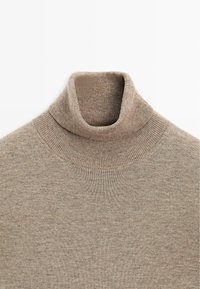 Pull à col roulé beige en tricot avec col côtelé et coutures aux épaules, posé à plat sur un fond blanc.