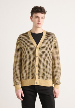 Knitted cardigan in golden yellow with small black openings, featuring a V-neck, button closure, and ribbed cuffs.
