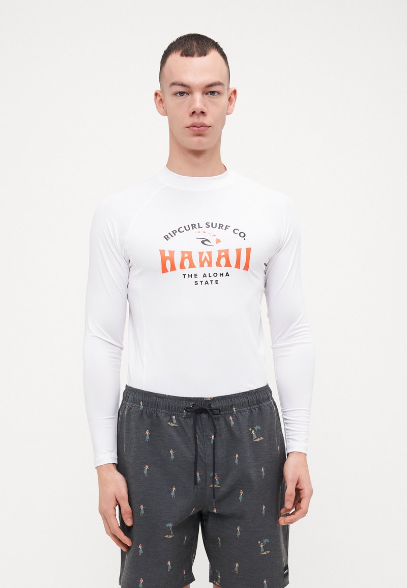 Biała rash guard z długim rękawem, z grafiką "Hawaii" w kolorze pomarańczowym i czarnym, w zestawie z ciemnymi szortami w tropikalny wzór.