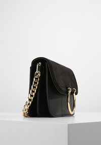 Borsa nera con pattina in camoscio e corpo in pelle, caratterizzata da una tracolla in catena dorata e un accent in metallo dorato circolare.