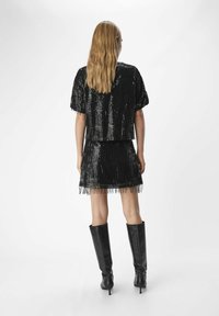 Completo due pezzi nero con paillettes, composto da un top corto e una mini gonna con dettagli a frange, abbinato a stivali neri con tacco alti fino al ginocchio.