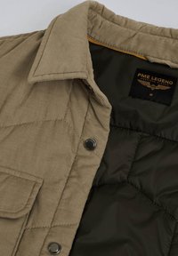 Chaqueta de pana beige con un forro acolchado en verde oscuro, que presenta una etiqueta con el logotipo "PME Legend" y botones de presión de metal en la parte delantera.