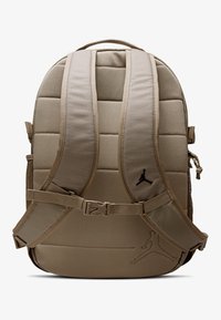 Beigefarbener Rucksack mit gepolsterten Trägern, Mesh-Akzenten, verstellbarer Schnalle und geprägtem Logo-Detail. Das Material wirkt robust und strukturiert.