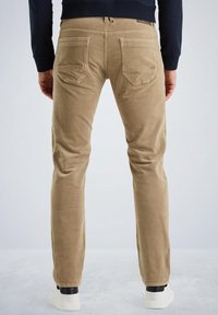Lichtbruine corduroy broeken met een rechte pasvorm, voorzien van achterzakken en subtiele stikseldetails. Gepaard met witte sneakers.