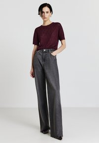 Top corto a maniche corte in maglia borgogna con motivo testurizzato abbinato a jeans di denim grigi a vita alta e gamba larga. Accessori minimalisti in argento.