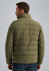 Olive green padded jacket with horizontal stitching detail, high collar, and long sleeves, worn over blue denim, viewed from the back.