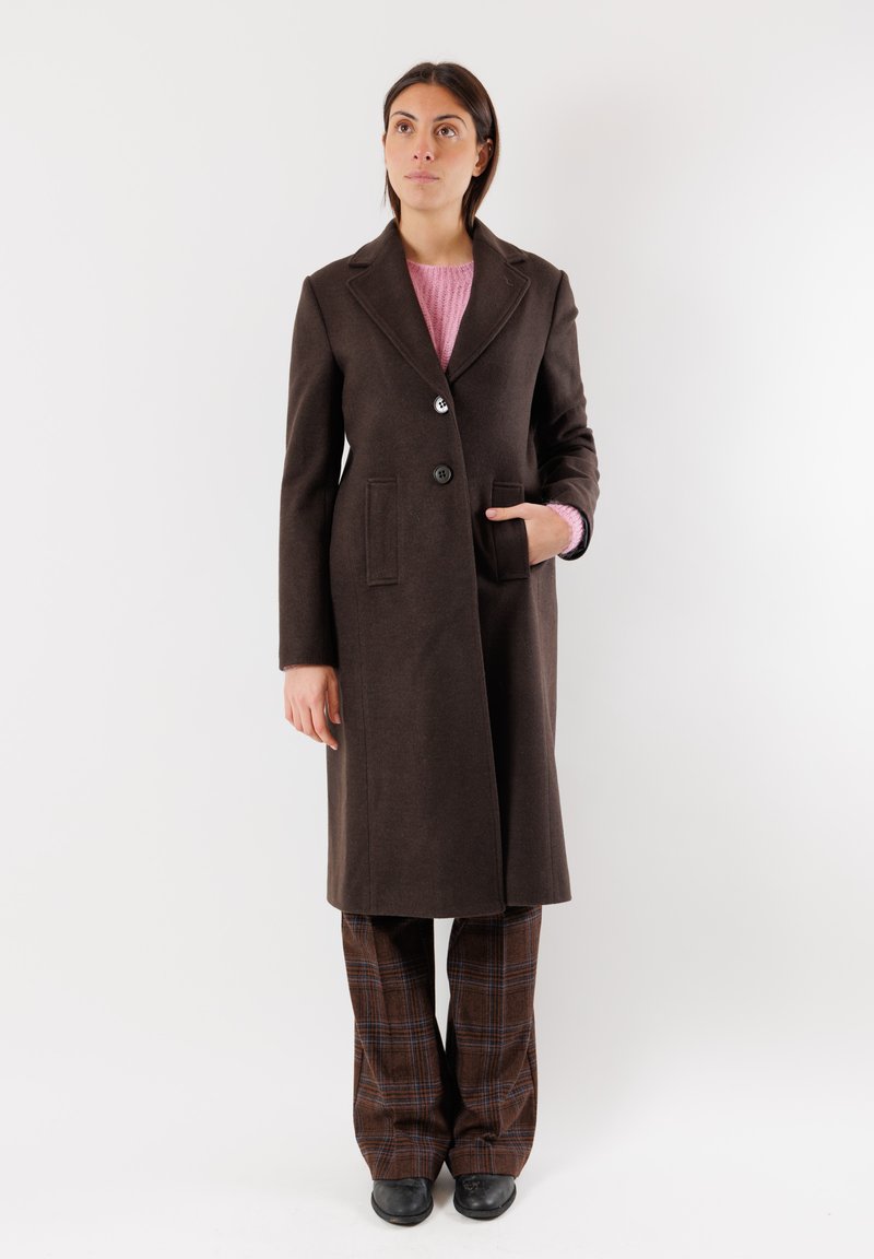 Cappotto di lana marrone con rever a punte, bottoni a singolo petto e due tasche laterali, indossato sopra un maglione rosa e pantaloni a quadri.