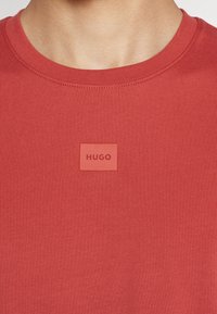 Czerwona koszulka z okrągłym dekoltem, wykonana z gładkiej bawełny, z teksturowanym kwadratowym naszywką z logo "HUGO" na piersi.
