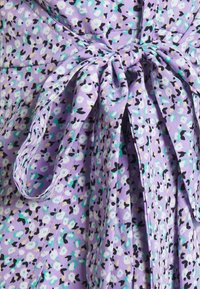 Tissu floral violet avec de petits motifs turquoise et blancs, présentant un détail noué en accent, fabriqué en matériau doux et léger.