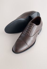 Pruunid nahast kleitkingad, millel on sile tekstuur, paelaga kinnitussüsteem, kapikujuline nina detail ja must kummist tallaga, millel on tekstuuriga haardepind.