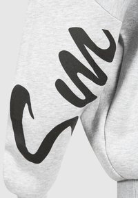 Sweat à capuche gris avec un design abstrait noir sur la manche. Fabriqué en tissu doux avec des poignets côtelés, il présente une texture lisse et une coupe décontractée.