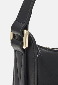 Musta nahkainen laukkunnauha, jossa on kultaiset metalliosat, sileä rakenne ja korostettu ommel kiinnityskohdassa.