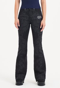 Schwarze Jeans mit Schlag, die über feine, tonale Stickereien mit wirbelnden Mustern verfügen. Hohe Taille und Fünf-Pocket-Design. Verstärkte Nähte.