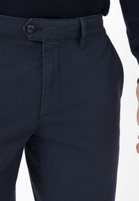 Chinos bleu marine en tissu mélangé coton, dotés d'une poche avant, d'une fermeture à bouton et d'une texture lisse avec des détails de couture minimaux.