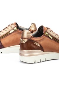 Zapatillas de cuero marrón y beis con acentos dorados, paneles texturizados, un zipper lateral y suela blanca; incluye tachuelas decorativas en el talón.