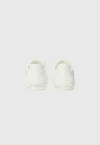 Hvite sneakers med en glatt, læraktig tekstur, som har en polstret krage og opphevet logo-detalj på hælen. Minimalistisk design.