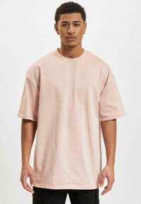 Lys rosa oversized T-shirt lavet af blødt stof. Korte ærmer, rund hals og en afslappet pasform uden synlige grafik eller mønstre.