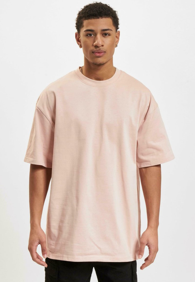 Lys rosa oversized T-shirt lavet af blødt stof. Korte ærmer, rund hals og en afslappet pasform uden synlige grafik eller mønstre.
