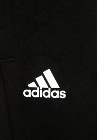 Zwarte textiel met een wit Adidas-logo. Het logo heeft drie diagonale strepen boven de merknaam in een vetgedrukt, schreefloos lettertype.