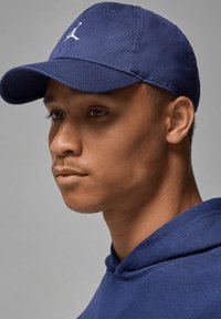 Marineblå baseballcaps med buet brem og brodert logo, brukt sammen med en matchende marineblå hettegenser, som viser et rent, teksturert stoff.