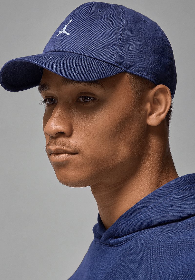 Marineblå baseballcaps med buet brem og brodert logo, brukt sammen med en matchende marineblå hettegenser, som viser et rent, teksturert stoff.