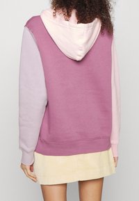Hoodie i lila och rosa färgblock, med en mjuk textur. Kombinerad med en ljusgul kordskjorts.