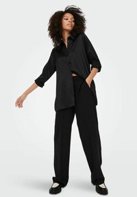 Camicetta nera con maniche arrotolate, vestibilità leggermente oversize. Abbina pantaloni neri a gamba larga e scarpe nere chunky. Tessuto liscio.