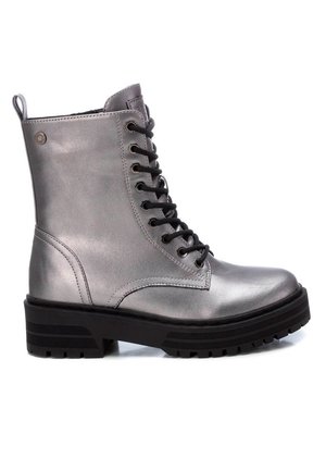 Botines metálicos plateados con cordones, suela de goma negra, punta redonda y cordones negros en contraste; cuenta con una lengüeta en el talón para facilitar el uso.