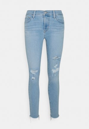Jean skinny bleu clair avec des déchirures usées sur le devant des cuisses et des ourlets effilochés, avec poches avant et passants pour ceinture.