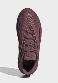 Burgundy träningsskor med texturerad ovandel, snören och förstärkt tåhätta. Har en framträdande logotyp på tungan och en smidig, böjd sula.