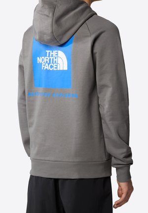 Harmaa huppari, jossa sininen suorakaiteen muotoinen logo, jossa lukee "THE NORTH FACE" ja "NEVER STOP EXPLORING." Pehmeä kangas, resorit hihansuissa ja helmassa.