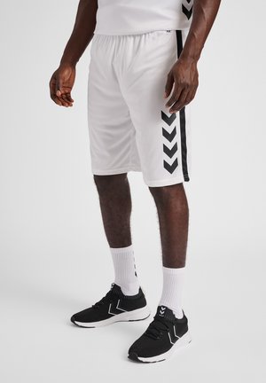 Hvide atletiske shorts har sorte chevron-striber på siderne. Kombinationen med sorte sneakers og hvide ankelsokker er designet til komfort.
