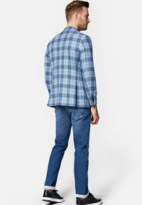 Jasnoniebieska marynarka w kratę o dopasowanym kroju, zestawiona z ciemnoniebieskimi dżinsami. Marynarka ma lekki połysk i ozdobne guziki. Czarne sneakersy.