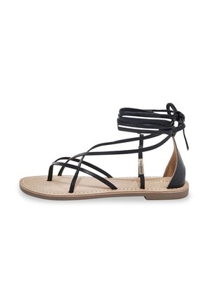 Sanda de gladiador de cuero negro que presenta múltiples correas, una suela plana y un diseño de tobillo atado. Plantilla beige con detalle de costura.