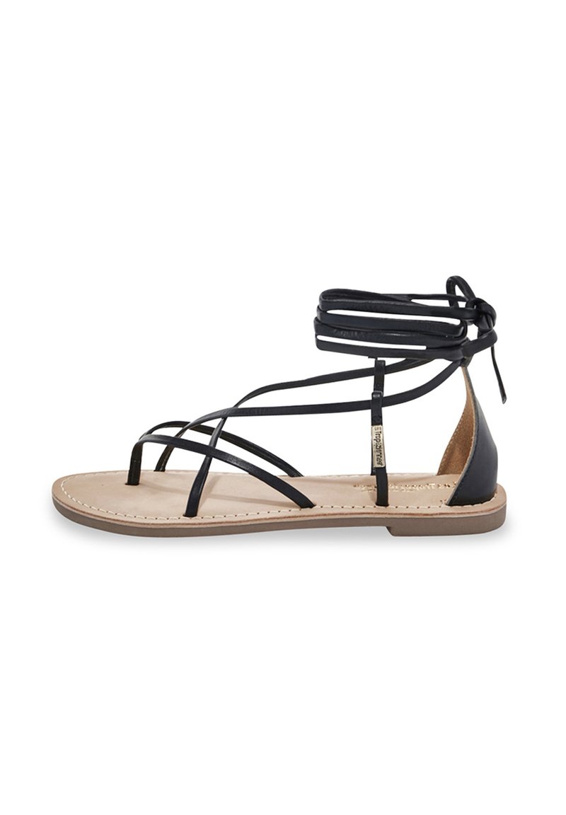 Sandale gladiateur en cuir noir avec plusieurs lanières, semelle plate et design lacé à la cheville. Semelle intérieure beige avec détails de couture.