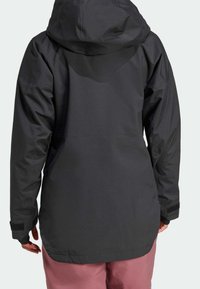 Veste noire imperméable avec capuche, dotée d'une texture lisse, de manches longues, de poignets ajustables et d'une coupe légèrement plus longue à l'arrière.