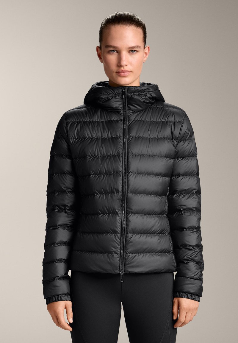 Črna puhovka s kapuco, ki ima kvadrataste sekcije, sprednji zadrgo in elastične manšete. Gladek, sijoč teksturiran material.