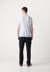 Camicetta azzurro chiaro a maniche corte con colletto e polsini a coste, abbinata a pantaloni scuri, che mostrano una texture liscia e un design aderente.