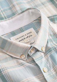Camicia a quadri azzurro chiaro e bianca realizzata in un morbido tessuto con colletto button-down, con accenti bianchi per i bottoni e un'etichetta del marchio.