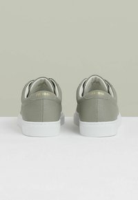 Adidași gri din piele cu o finișare texturată, talpă din cauciuc alb și litere aurii pe călcâie. Vedere din spate, design minim.