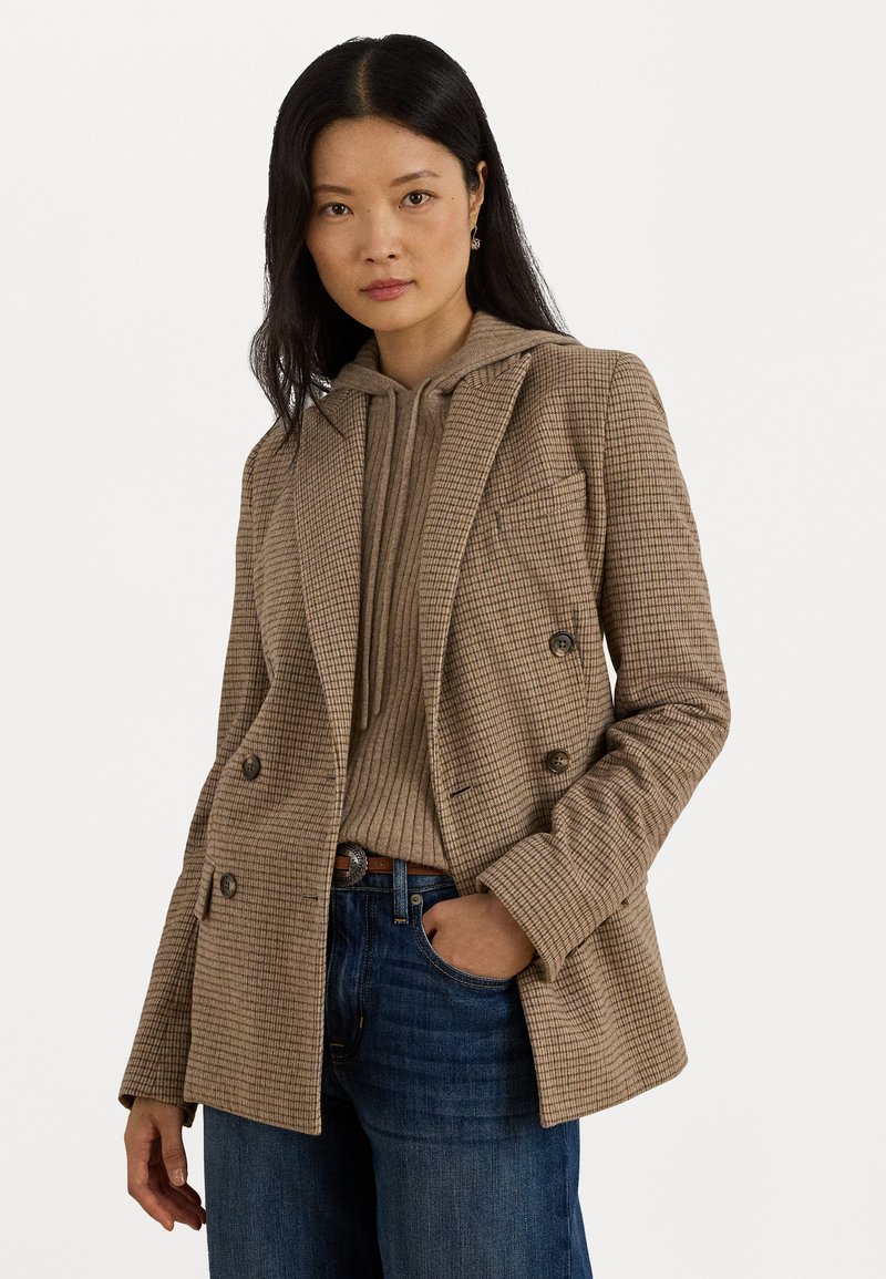 Bruine houndstooth dubbelzijdige blazer met pieklapels, voorzakken en textiele voering, gedragen over een tan hoodie en blauwe jeans.