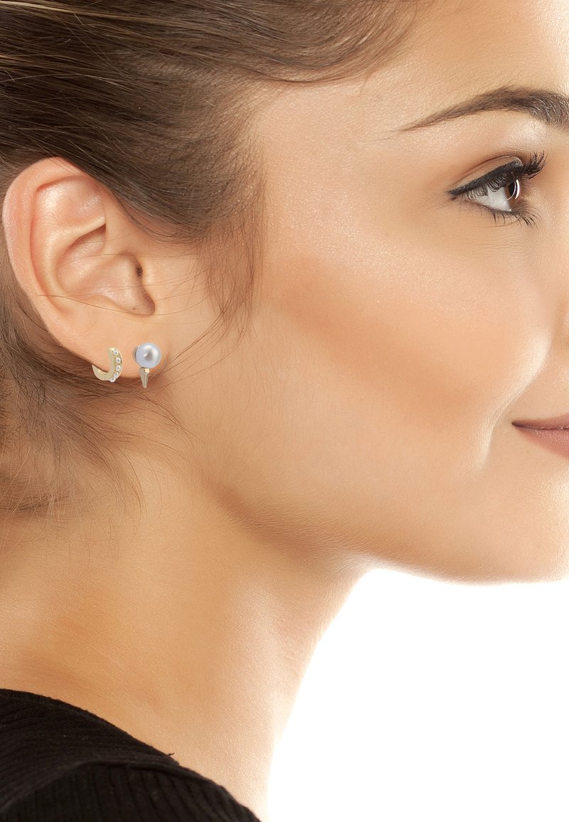 Gold-tone earrings featuring a crescent shape adorned with small gemstones and a pearl stud; showcased on a woman's ear with a neutral background.