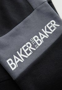 Sekcja czarno-szara z bluzą, z wyraźnym białym logo "BAKER by TED BAKER" w pogrubionej czcionce. Miękki, teksturowany materiał.