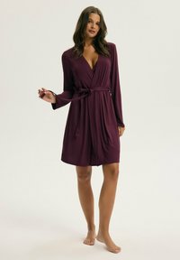 Bordowa sukienka w stylu wrap z długimi rękawami, dekoltem w serek i paskiem w talii. Miękka tkanina z korzystnym układem, sięgająca do połowy uda.