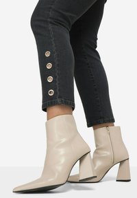Beige leren enkellaarsjes met een spitse neus en een chunky hak. Gecombineerd met donkerdenim jeans met messing grommets op de zoom.