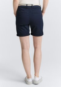 Marineblaue Shorts mit aufgerolltem Saum, glatter Textur, Gesäßtaschen und einem taillierten Bund, kombiniert mit weißen Streifen-Sneakern.
