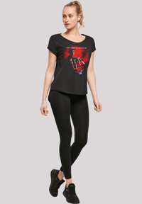 Svart grafisk t-skjorte med et skrekk-tema print, kombinert med svarte leggings og sneakers. T-skjorten har en avslappet passform og rund hals.